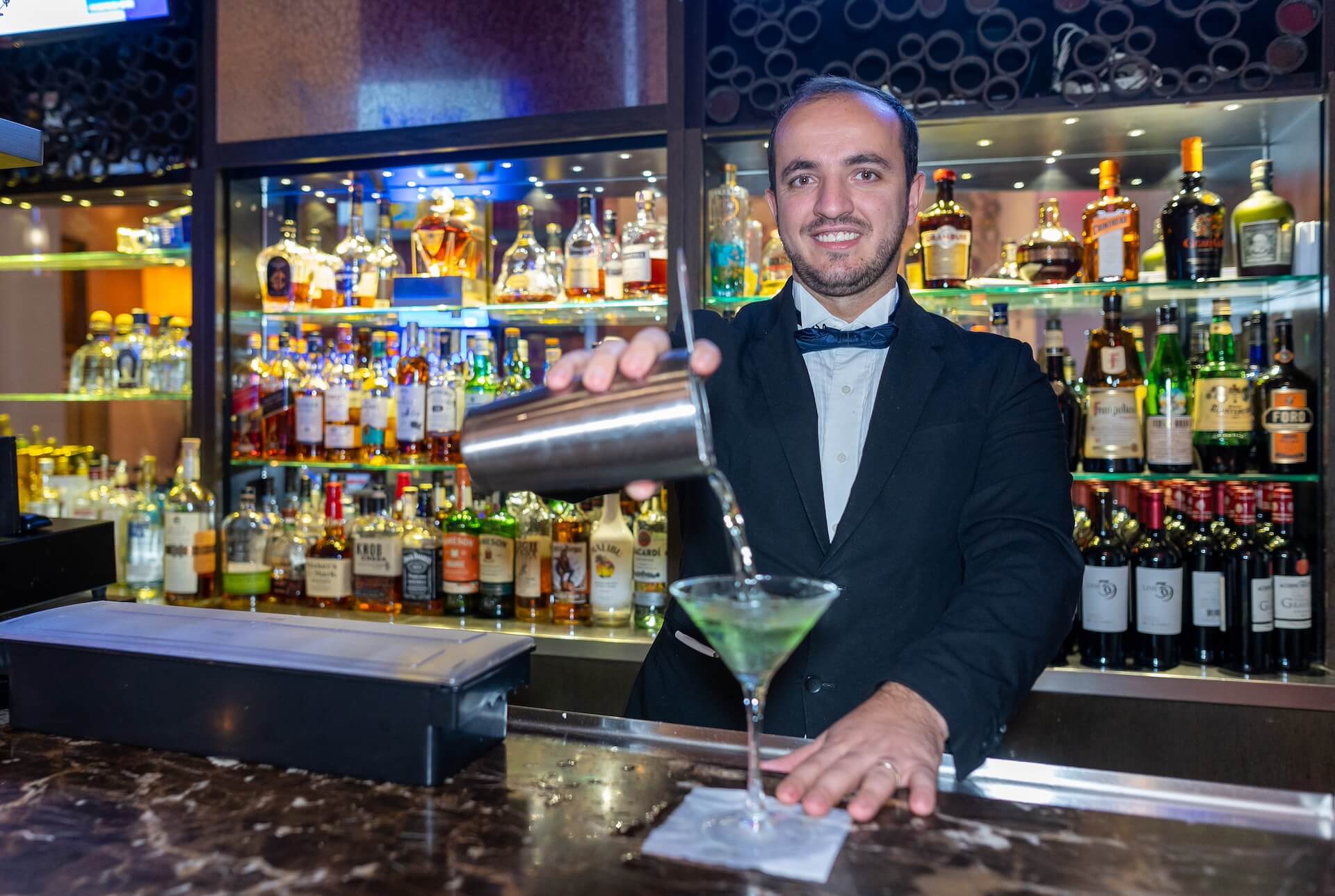 Bartender pouring green drink into a martini glass